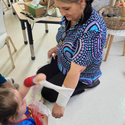 educator and child doing bandaging junior safety and wellbeing. Staying up to date with workplace training is important for personal and professional development.