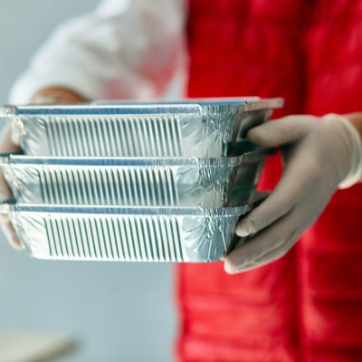 Person wearing gloves holding stacked foil food containers for food safety practices in the hospitality industry