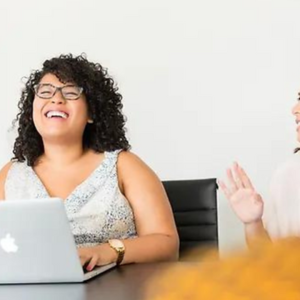 smiling women using a laptop at a table. Manage workplace stress