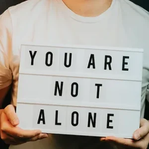 person holding you are not alone sign. Our programs and courses about mental health help reduce mental health stigma. Supporting people with mental health is important to us.